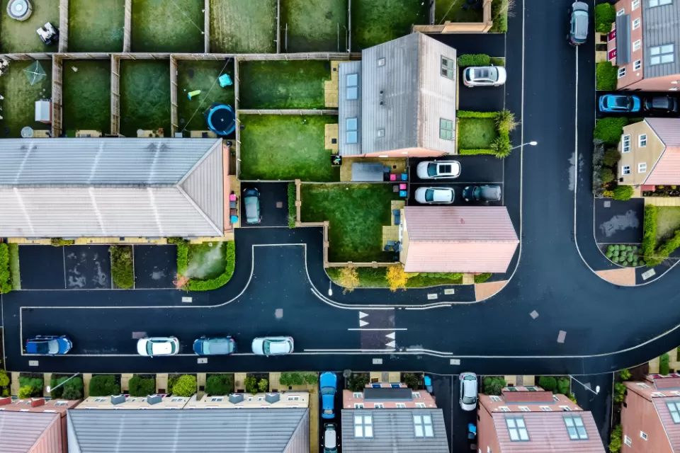 A suburban street in England, shown directly from above, with lush, green yards and driveways with cars parked in front.